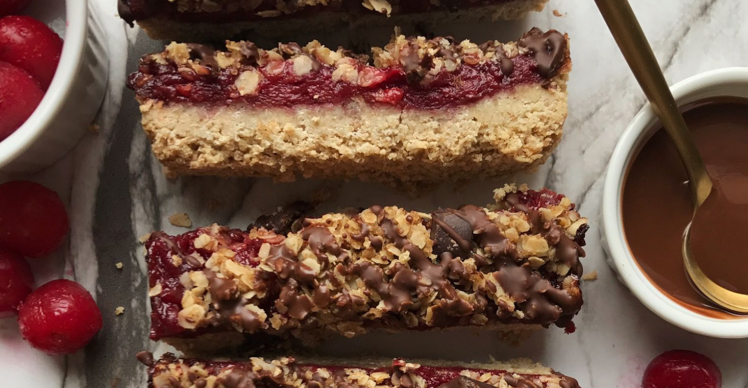 A close up of chocolate cherry dessert bars with whole cherries and chocolate sauce on the side.