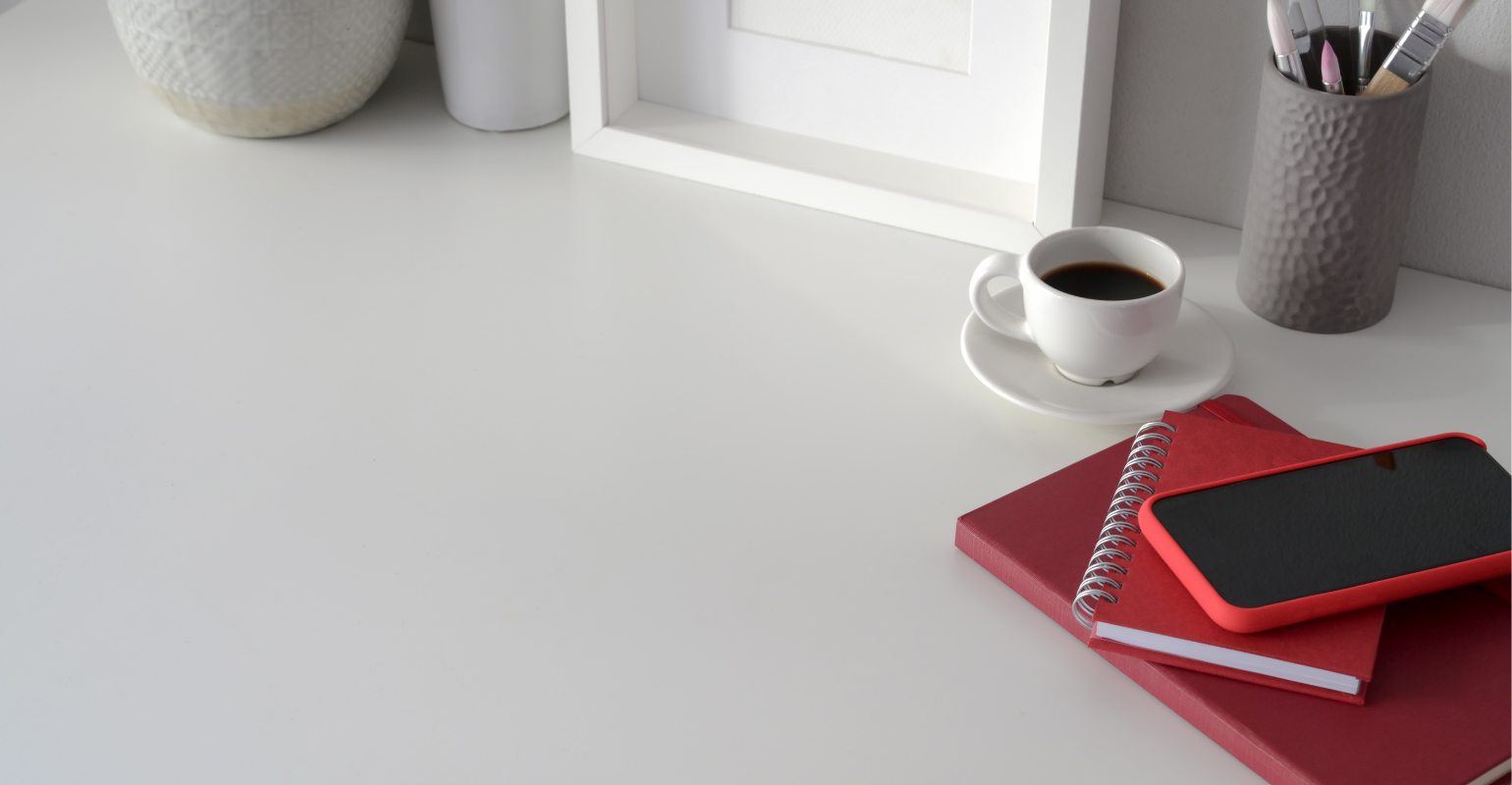 An immaculate white desk with coffee cup, paint brushes, notebooks, and cell phone tucked in the top right corner.